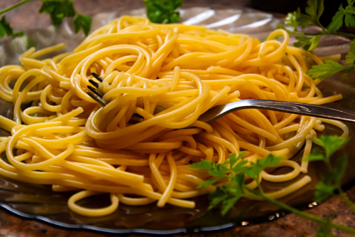 A plate of cooked spaghetti noodles with fork and a parsley garnish.